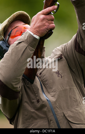 L'homme à tirer sur une simulation de tir jeu de tir d'argile portant chapeau de tweed, de l'oreille et des lunettes de protection Banque D'Images