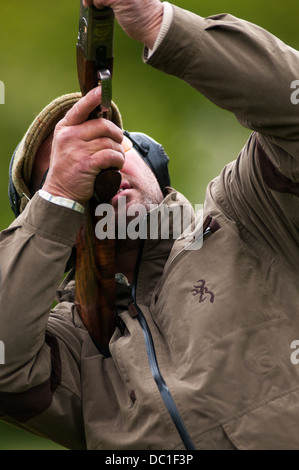 L'homme à tirer sur une simulation de tir jeu de tir d'argile portant chapeau de tweed, de l'oreille et des lunettes de protection Banque D'Images