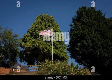 Union Jack battant fièrement devant de grands arbres Leylandii dans un jardin à Horning sur les Norfolk Broads (plus de légende dans la description ..). Banque D'Images