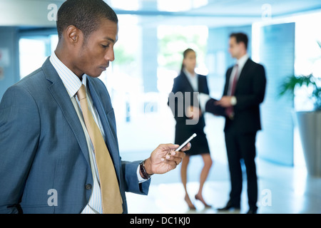 Businessman text messaging with cell phone in lobby Banque D'Images