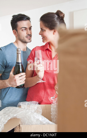 Les jeunes couples célébrant avec champagne parmi les boîtes de carton Banque D'Images