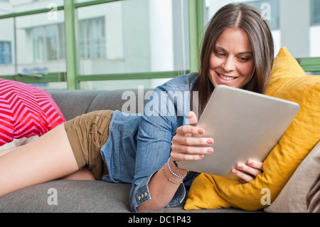 Young woman lying on sofa holding digital tablet Banque D'Images