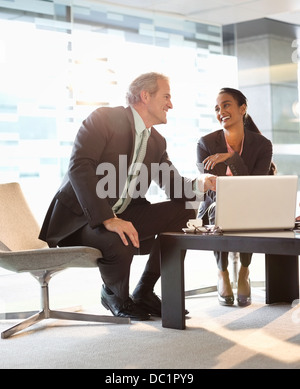 Smiling businessman and businesswoman using laptop in lobby Banque D'Images