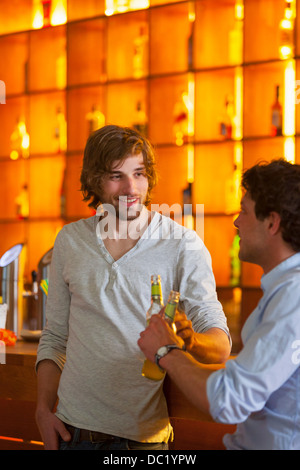 Deux hommes debout au bar avec des bouteilles de bière Banque D'Images