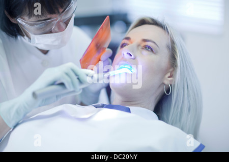 Femme dentiste en utilisant la lumière ultraviolette sur les dents des patients Banque D'Images