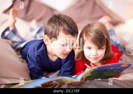 Deux jeunes enfants lying on bed looking at photo book Banque D'Images