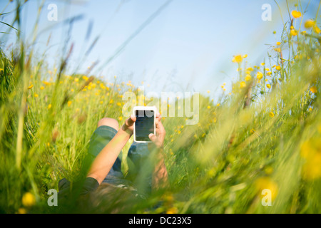 Garçon couché dans l'herbe haute à jouer sur smartphone Banque D'Images