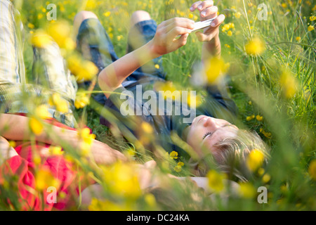 Garçons couchés dans l'herbe haute à jouer sur smartphone Banque D'Images