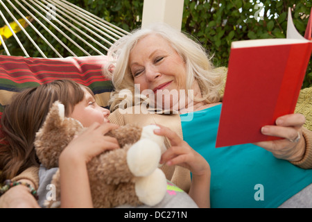 Grand-mère et petite-fille reading book in hammock Banque D'Images