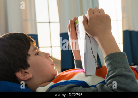 Boy lying on bed reading book Banque D'Images