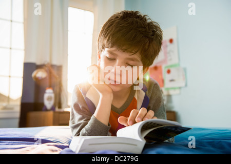 Boy lying on bed reading book Banque D'Images