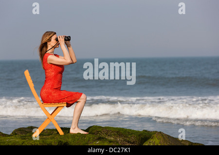 Mature Woman sitting on chair on beach with binoculars Banque D'Images