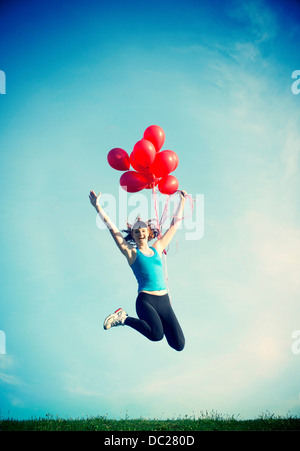 Teenage girl jumping in mid air holding red balloons Banque D'Images
