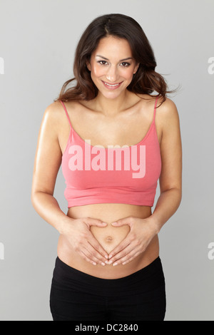 Pregnant woman making heart shape avec les mains sur l'estomac Banque D'Images