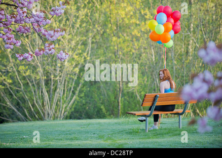 Teenage girl sitting on park bench with balloons Banque D'Images