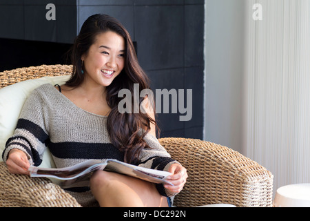 Portrait de jeune femme assise sur un fauteuil avec magazine Banque D'Images