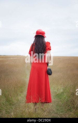 Une femme en robe rouge est de marcher sur un champ Banque D'Images