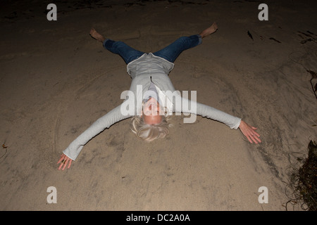 Young woman lying on sand avec bras et jambes Banque D'Images