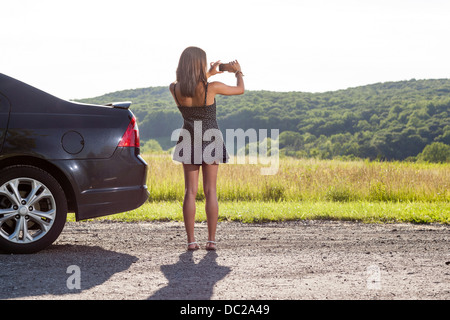 Young woman photographing rural scene with camera phone Banque D'Images