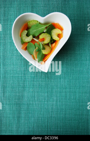 Salade de légumes divers en forme de coeur bol sur fond vert, de l'espace libre pour le texte Banque D'Images