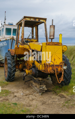 Un ancien tracteur jaune rouillé, manque une roue avant. Il a été utilisé pour remorquer des bateaux sur le rivage dans l'estuaire de la Humber. Banque D'Images
