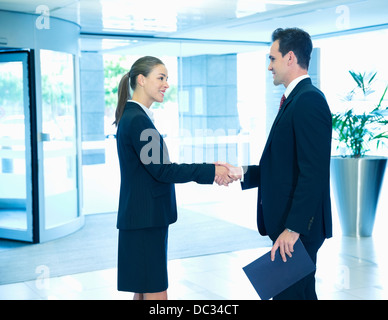 Smiling businessman and businesswoman handshaking in lobby Banque D'Images