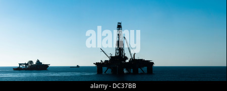 Silhouette d'une plate-forme pétrolière en zone extracôtière, dos dur lumière, ciel bleu, refelection sur surface de l'eau. Banque D'Images
