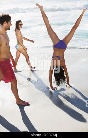 Friends watching woman in bikini doing handstand on beach Banque D'Images