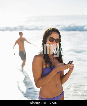 Portrait of smiling woman in bikini with cell phone on beach Banque D'Images