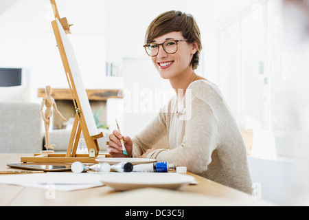 Portrait of smiling woman painting at easel on table Banque D'Images