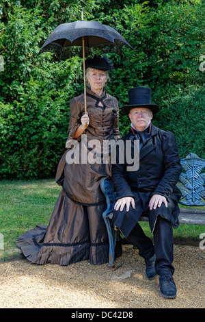 Loisirs : gentleman victorien dans top hat & double breasted redingote avec dame en robe avec agitation dans hat sous un parasol Banque D'Images