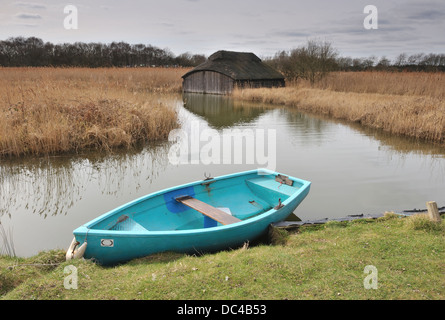 Bleu bateau avec un toit traditionnel en chaume maison bateau en arrière-plan, Norfolk Broads, UK Banque D'Images