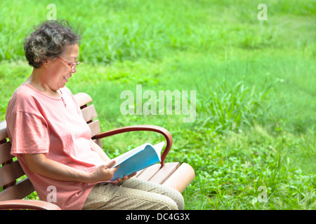 Happy senior femme assis sur un banc et la lecture d'un livre Banque D'Images