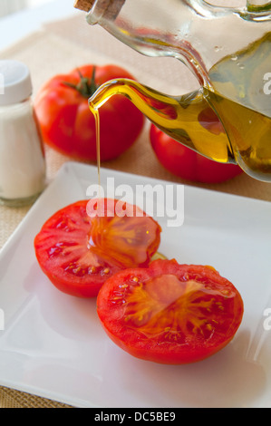 Bouteille d'huile verser l'huile d'olive sur une de tranches de tomate. Banque D'Images