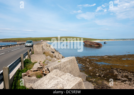 Une voiture en traversant la barrière Churchill 3 avec les restes d'un blockship entre Glimps Holm et Burray, Orkney. Banque D'Images