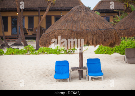 Plage bleu chaises longues sous les parasols en chaume sur une plage des pluies Banque D'Images