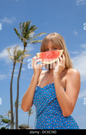 Une femme montre une tranche de melon d'en face de son visage. Banque D'Images