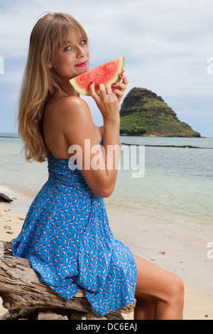 Une blonde woman mange de la pastèque à hawaii. Banque D'Images