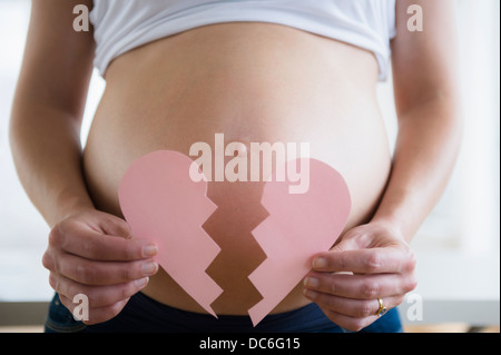 Mid section of pregnant woman holding papier coeur brisé Banque D'Images