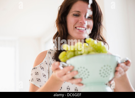 Portrait of young woman washing grapes in colander Banque D'Images