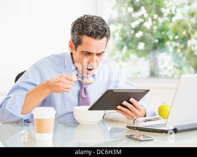 Portrait of man eating and using digital tablet Banque D'Images