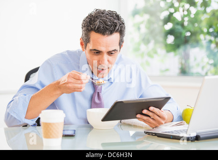 Portrait of man eating and using digital tablet Banque D'Images
