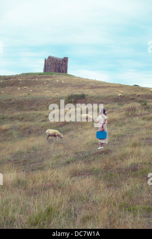 Une fille dans une robe vintage sur une prairie avec moutons, dans l'arrière-plan d'une chapelle Banque D'Images