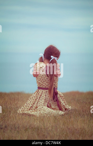 Jeune fille dans une robe vintage, assis sur un pré, serrant elle-même Banque D'Images