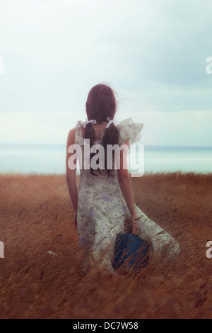 Une fille dans une robe à fleurs sur un champ avec une valise Banque D'Images