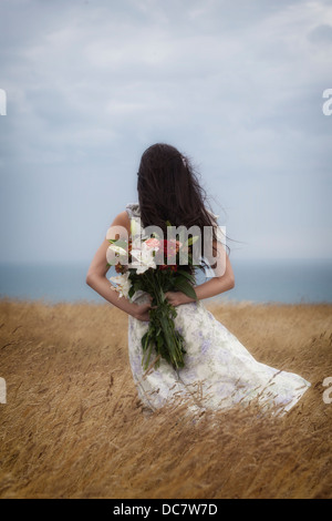 Une fille dans une robe à fleurs avec un bouquet de fleurs sur un champ Banque D'Images