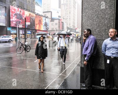 2 hommes d'attendre la fin de la pluie sous abri en tant que piétons pressés le long de Broadway dans une grave tempête Theatre district New York Banque D'Images