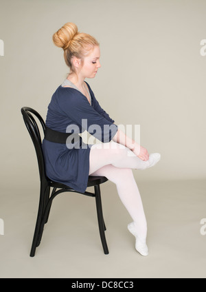 Jeune femme blonde en robe de ballet adolescent assis sur une chaise le massage pied Banque D'Images