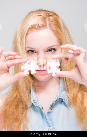 Jeune blond woman holding et l'examen de deux pièces de puzzle blanc Banque D'Images