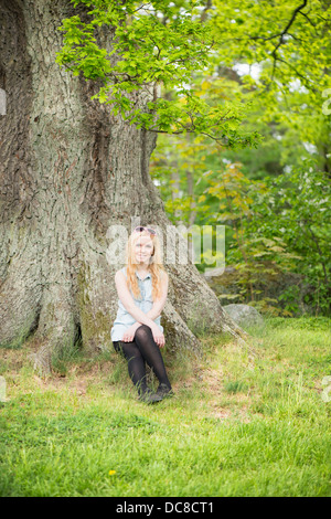 Scène de la nature avec l'un young attractive woman sitting by a tree in a park Banque D'Images